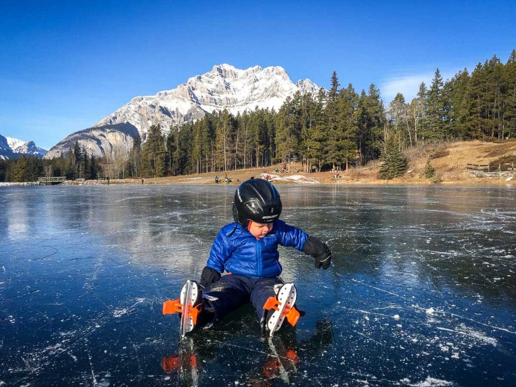 small child sitting on ice - skating on Johnson Lake in Banff.