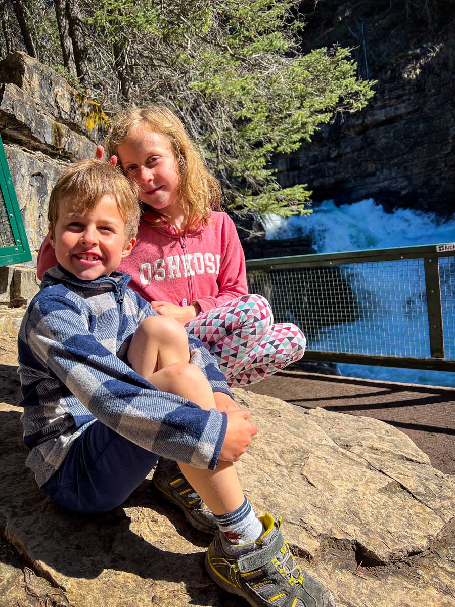 two kids sitting in front of a waterfall along the Johnston Canyon hike.