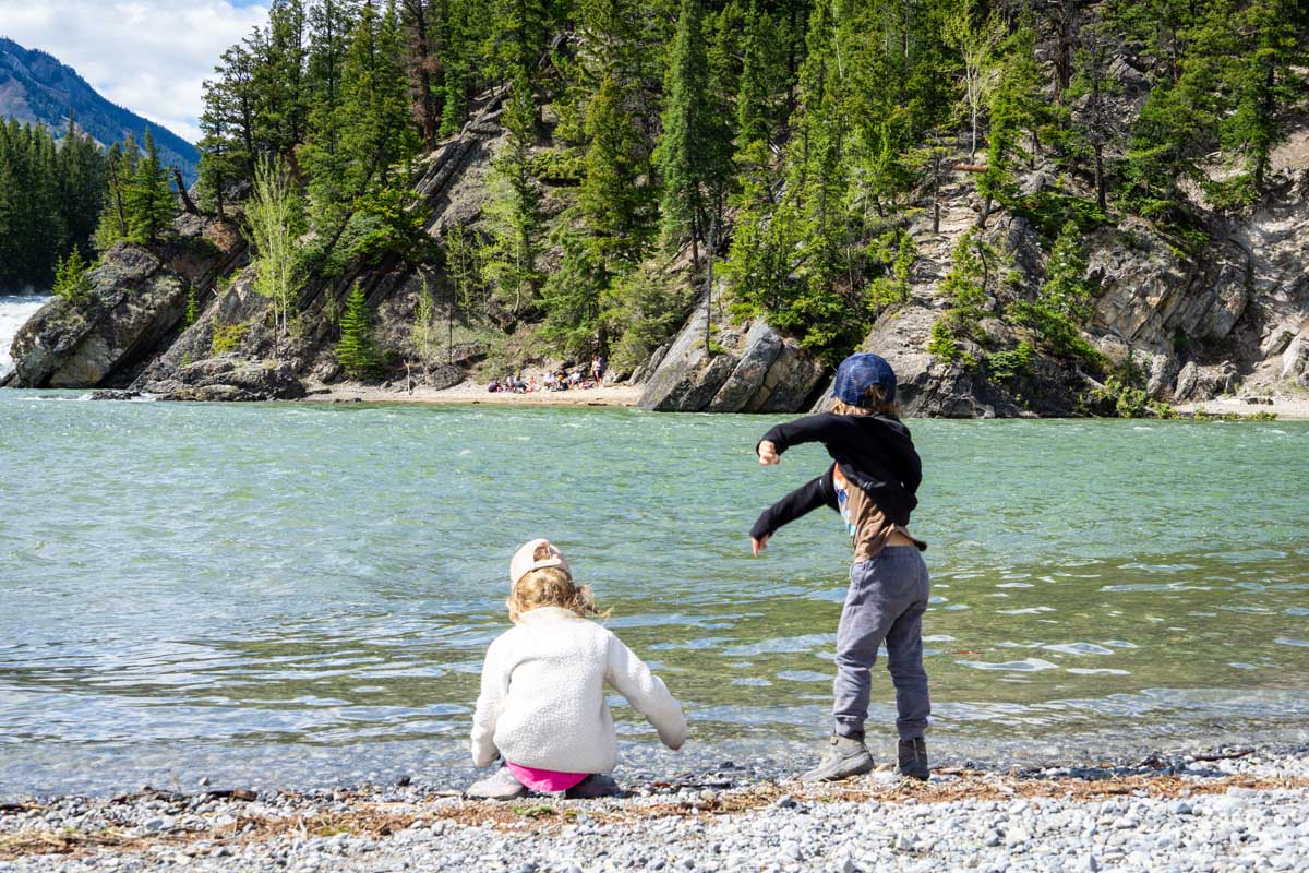 two kids throw rocks into the Bow River in Banff.