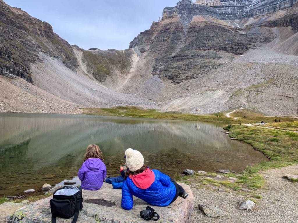a mother and two kids sit on a rock after hiking to Minnestimma Lakes from Moraine Lake in Banff.