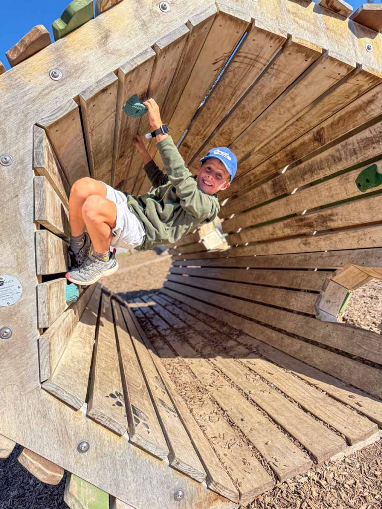 a 10-year old boy plays in a wooden tunnel with climbing handles at the Banff Elementary School playground.
