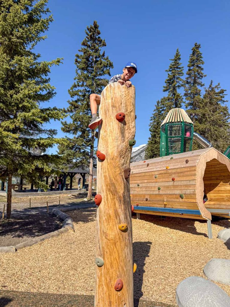a 10-year old boy climbs a wide wooden post at the Sundance Playground - the best playground in Banff.