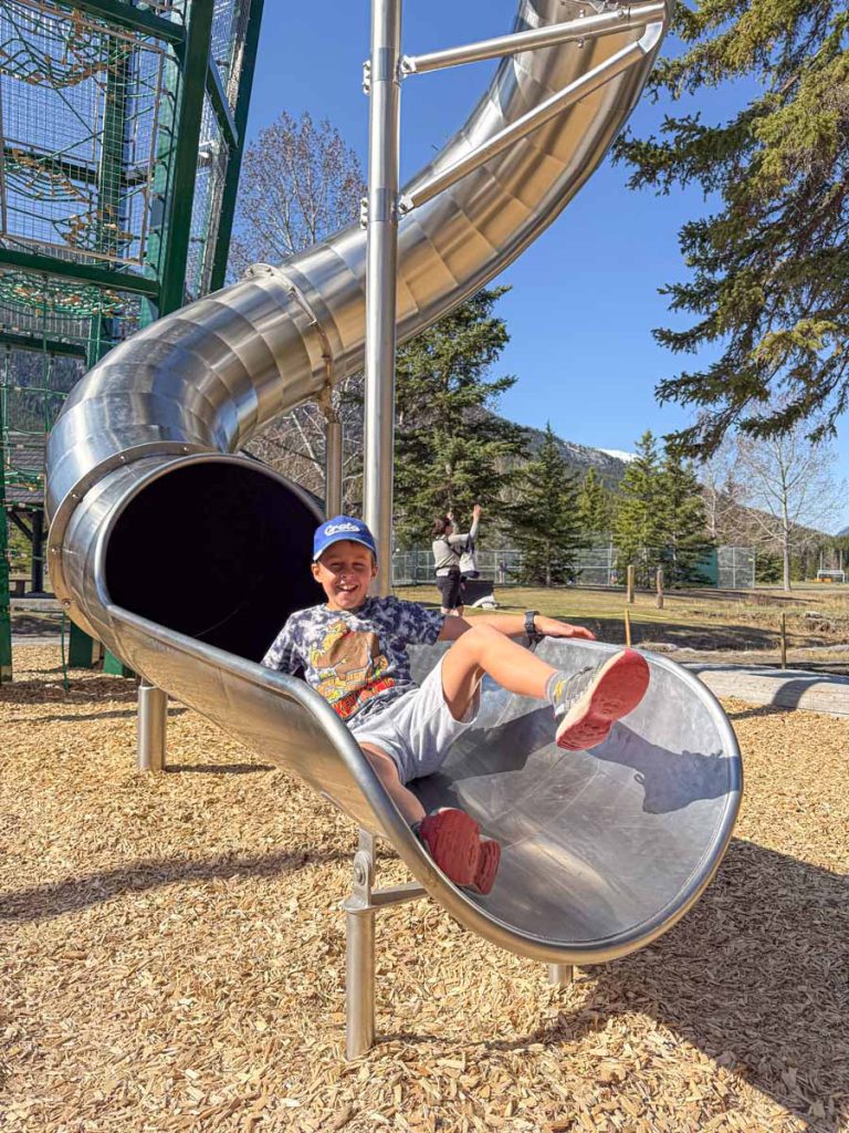 a 10-year old boy from the Banffwithkids.com family, is all smiles as he slides down the tall spiral slide at the Sundance Playground in the Town of Banff.